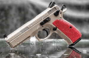 Close-up of a silver handgun with red grips on a reflective surface.